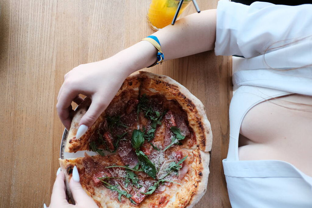 A mouthwatering view of a delectable Prosciutto Pizza topped with tomatoes, cheese, and arugula, elegantly presented on a rustic wooden table. - Zdjęcie, obraz