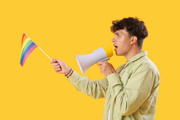 Junger Mann mit LGBT-Flagge brüllt in Megafon auf gelbem Hintergrund - Foto, Bild