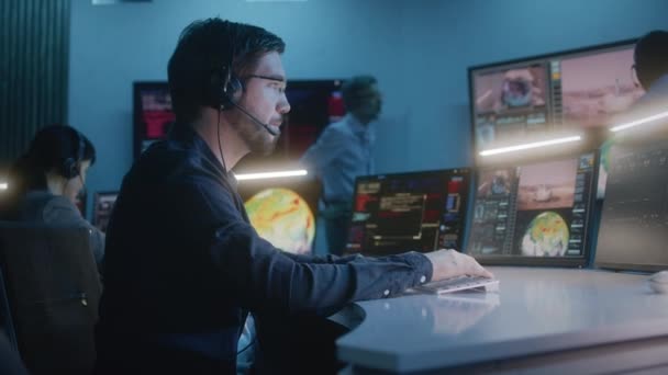 Flight control operator in headset sits in front of computers in mission control center, monitors space mission. Group of workers clap hands after spacecraft lift off displayed on big digital screens. - Footage, Video