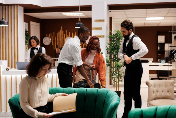 Hotel concierge asszisztál vendégek előtérben, segít a bejelentkezési folyamat a recepción. Bellboy szállító kocsi táskák és poggyász a szobába, így luxus szolgáltatást a modern üdülőhelyen. - Fotó, kép