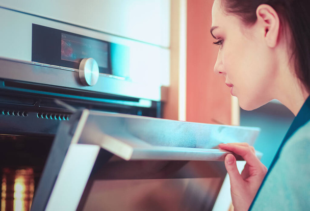 Beautiful young woman checking how her cake is doing in the oven. - 写真・画像