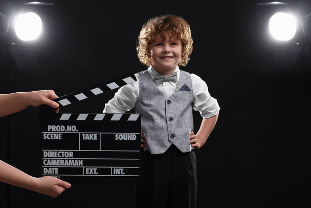 Smiling cute boy performing while second assistant camera holding clapperboard on stage. Little actor - Foto, afbeelding