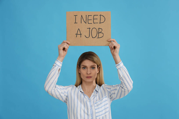 Безработная женщина держит табличку с фразой Мне нужна работа на светло-голубом фоне - Фото, изображение