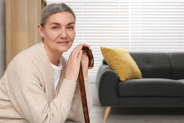 Senior woman with walking cane sitting on armchair at home. Space for text - Fotoğraf, Görsel
