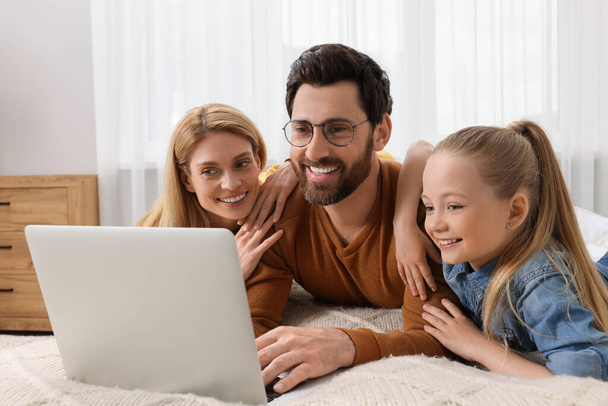 Happy family with laptop on bed at home - Fotó, kép