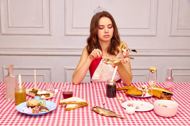 Retrato de una hermosa joven sentada en la mesa, celebrando su cumpleaños, comiendo pescado. Aperitivos extraordinarios. Concepto de fiesta, celebración, emociones, belleza femenina, juventud. Arte pop - Foto, imagen