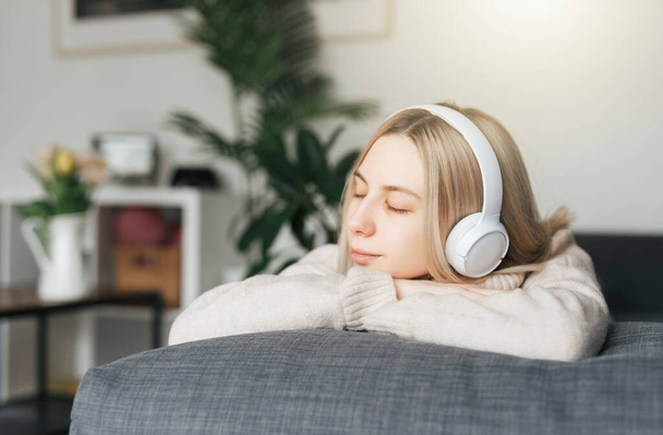 Young blonde woman in headphones listening to music and relaxing at home. - Φωτογραφία, εικόνα