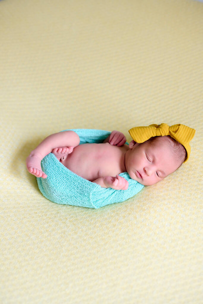Close-up of a newborn baby girl, inside a ball of blue wool on a yellow blanket with a yellow bow on her head, sleeping and laughing. - Photo, Image