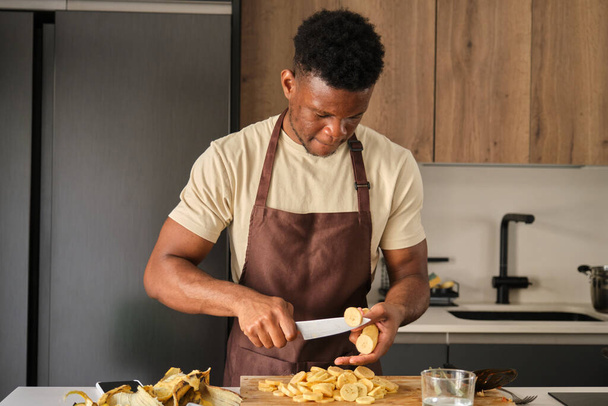 Young black man cutting plantains in a kitchen. - Zdjęcie, obraz