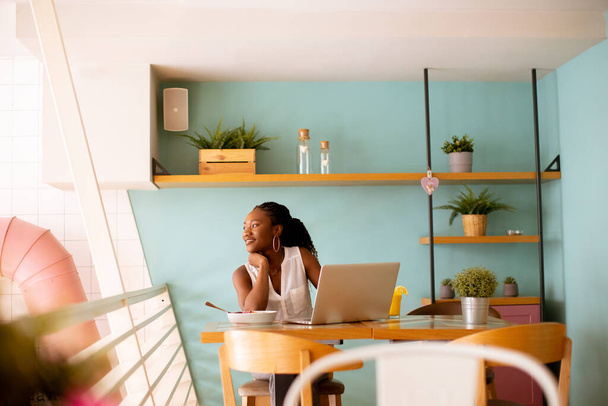 Pretty young black woman having a healthy breakfast while working on laptop in the cafe - Fotoğraf, Görsel