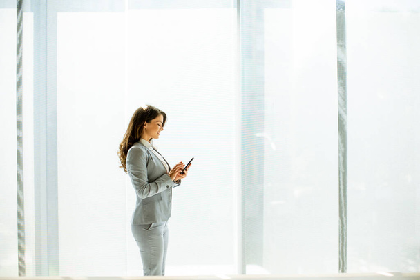 Красивая молодая женщина с мобильного телефона у окна офиса - Фото, изображение