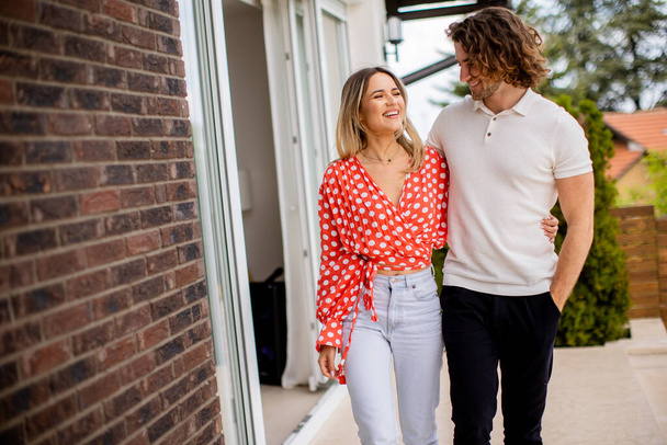 Bonito sorrindo jovem casal apaixonado andando na frente da parede de tijolo da casa - Foto, Imagem