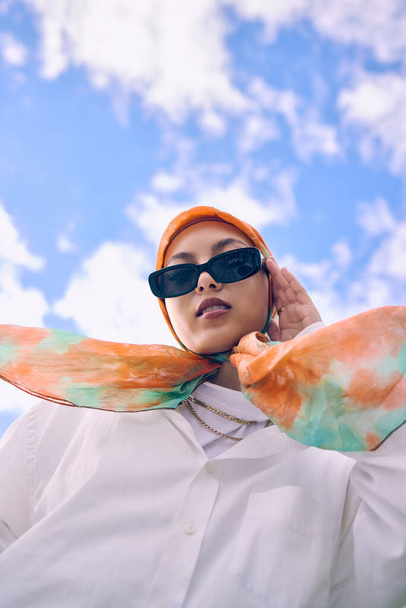 Портрет, мода или хиджаб с женщиной-сауди на открытом воздухе на голубом фоне неба в шарфе и солнечных очках для стиля. Мусульманин, вера или религия с модным молодым арабом на улице в современной одежде. - Фото, изображение