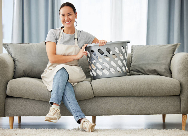 Happy asian woman, laundry and sofa for housekeeping, cleaning or hygiene in living room at home. Portrait of female person, cleaner or domestic with smile for clean clothing or washing on couch. - Photo, image