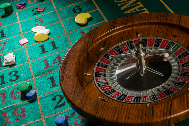 Wooden roulette wheel isolated over a green gaming table with colorful chips - Photo, Image