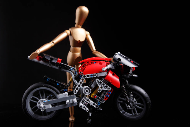 Кальяри, Италия - 12 января 2011: Деревянная кукла перевозит мотоцикл, построенный из лего, изолированный на черном фоне - Фото, изображение