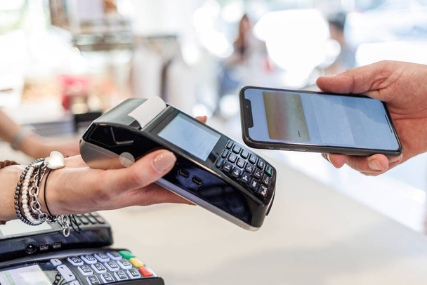 Dettaglio del pagamento con carta di credito con smartphone verso il pos tenuto per mano da una commessa - Foto, immagini
