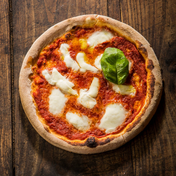 Pizza margherita coupé avec un coin tiré d'en haut isolé sur une table en bois - Photo, image