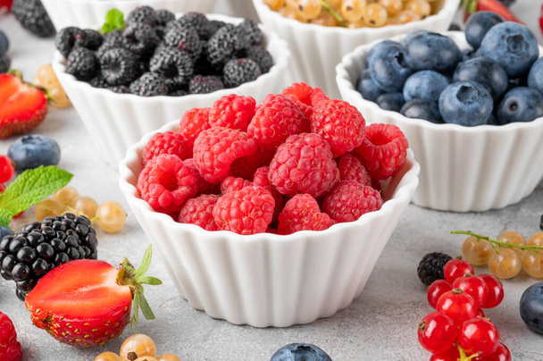 Various fresh berries in bowls on a gray concrete background. Healthy food concept - Fotó, kép