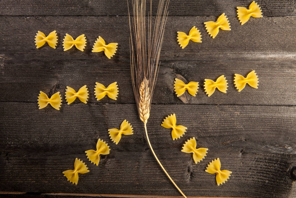 compositie met korte pasta en tarweoren op een donkere tafel - Foto, afbeelding