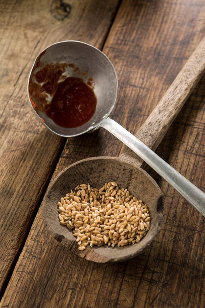 Пшеница на древнем ковше и томатный соус на металлическом ковше изолированы на деревянном столе - Фото, изображение