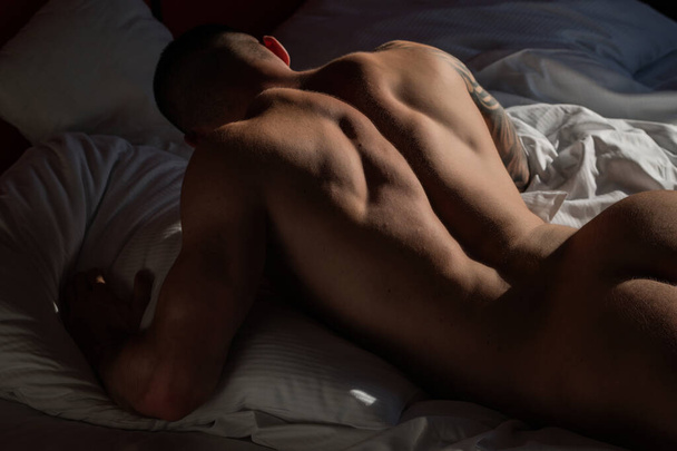 Sexy male round buttocks, Sexy shape butt. Muscular hunk. Naked man model in bed. Gay sexy model. Perfect shoulders and chest. Muscular sexy man with naked torso. Hunk with athletic body in bed - Foto, afbeelding