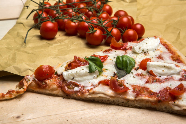 Detalle de una cuña de pizza con tomate y mozzarella sobre una mesa de madera - Foto, imagen