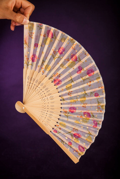Hand fan with floral designs on a dark purple background - Фото, изображение