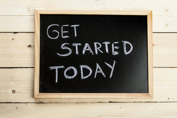 Black chalkboard on wooden background with the inscription: "get started today" - Zdjęcie, obraz