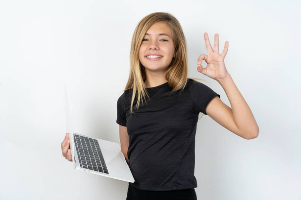 Gyönyörű kaukázusi tini lány visel fekete póló gazdaság netbook és bemutató okey szimbólum   - Fotó, kép