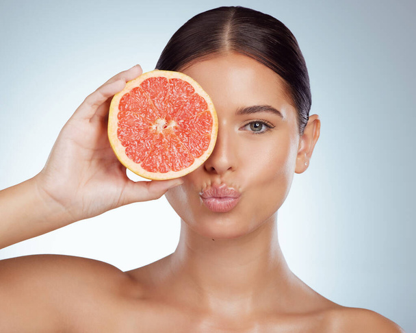 Face kiss, skincare and woman with grapefruit in studio isolated on white background. Portrait, natural or female model with fruit for vitamin c, nutrition or healthy diet, wellness or cosmetics pout. - Foto, afbeelding