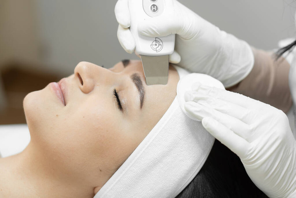 Sensación de frescura y rejuvenecimiento: limpieza facial ultrasónica de un cosmetólogo profesional para cuidar la salud de la piel. Relajación y relajación en el salón de belleza. Mujer disfrutando procedimiento en - Foto, imagen