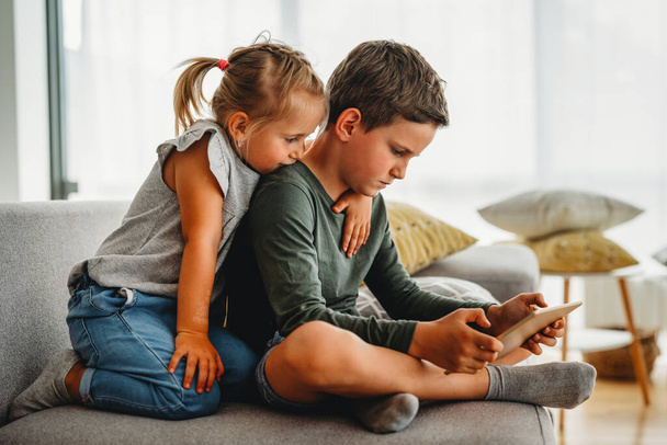Little girl and boy watching video or playing games on their digital device tablet, smartphone. Children digital addiction concept. - Fotó, kép