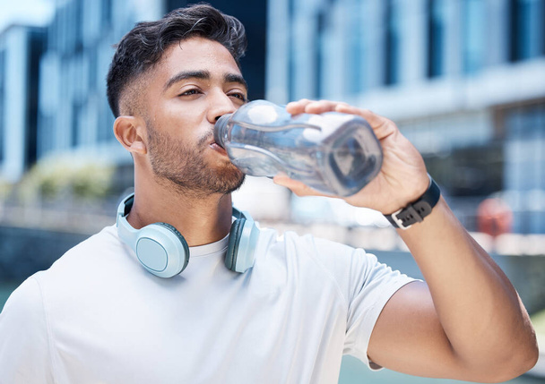Man, fitness and drinking water in city after exercise, cardio workout or training outdoors. Thirsty male person, athlete or runner with drink for hydration, rest or break from run in an urban town. - Foto, Imagen
