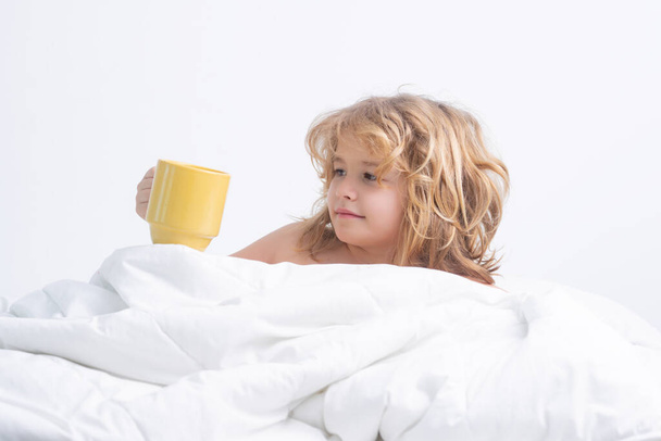 Morning drink. Kid with cup in bed. Portrait of little child lying on big bed. Concept of happy children having good time at home. Child awaked up in bed - Fotó, kép