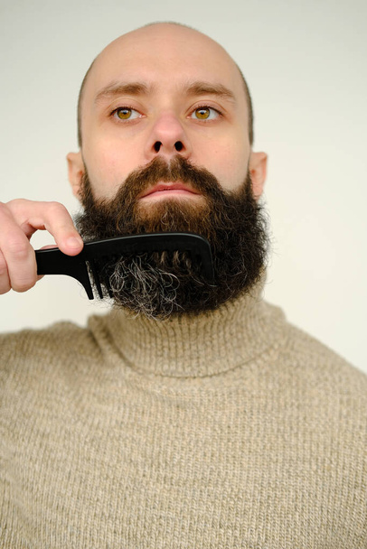close-up of male face, young bearded and mustachioed man, guy with 25 - 30 years combs his thick beard, concept of mustache and beard stubble care products, hairline hygiene on lower part of face - Фото, изображение