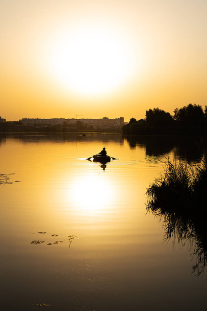 Nuori mies kalastaa järvellä puhallettavasta pienestä veneestä hyvin kauniissa oranssissa auringonlaskussa. - Valokuva, kuva