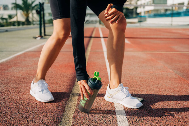 Nahaufnahme der Läuferbeine, auf der Straße stehen und sich nach dem Sport entspannen. Wassermixer-Flasche halten beim Workout in der sommerlichen City Street. - Foto, Bild