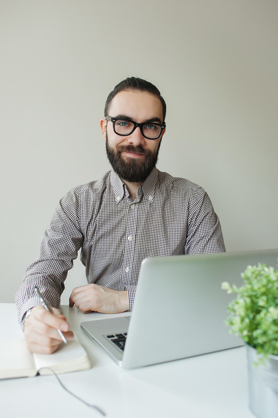 Homme souriant avec barbe dans des lunettes prendre des notes avec ordinateur portable notep
 - Photo, image