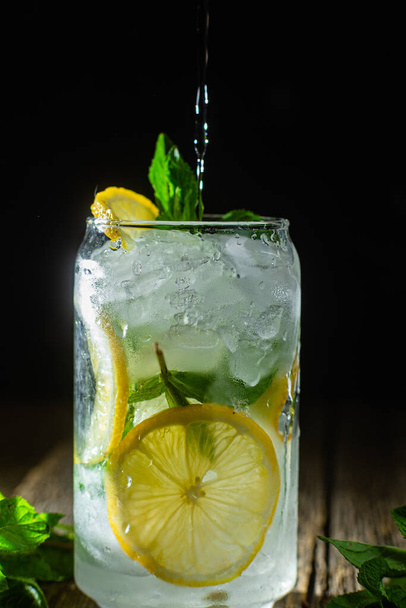 Cold lemonade with mint and lemon and ice on a dark background - Фото, изображение
