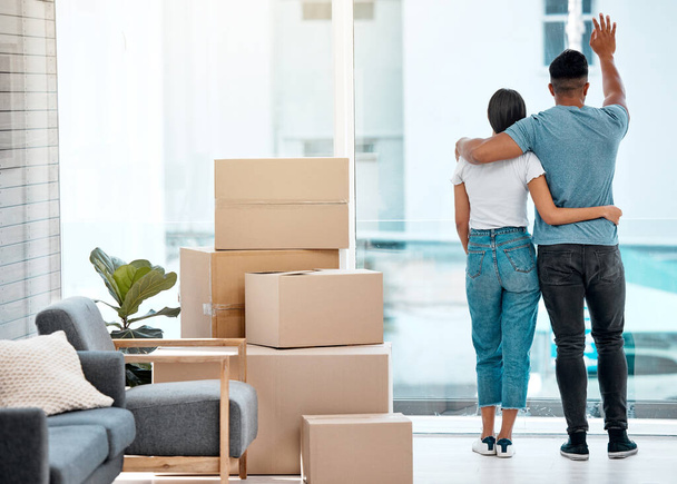 Box, hug and back of couple in new home for property, apartment and real estate investment. Relationship, house and man and woman wave hello to neighbour, embrace and boxes for moving day by a window. - Fotoğraf, Görsel
