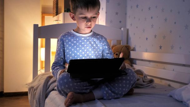 Petit garçon utilisant une tablette dans sa chambre la nuit. Éducation des enfants, développement, enfants utilisant des gadgets secret, vie privée. - Photo, image