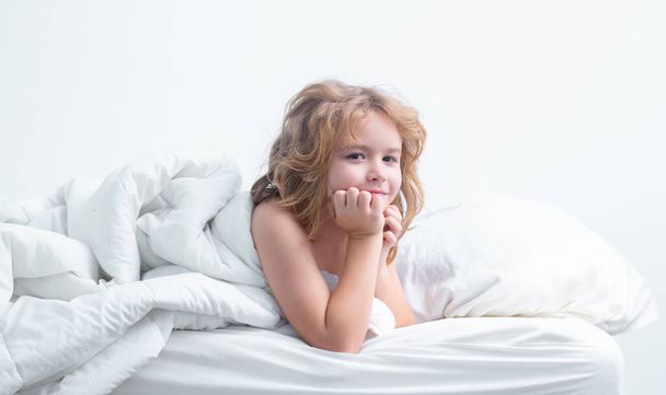 Child enjoys sunny morning. Good time at home. Kid wakes up from sleep. Child wakes up in morning in bed. Morning awakening little child in bed - Photo, Image