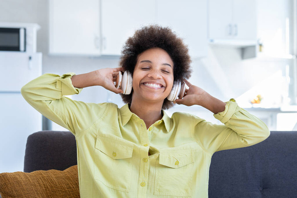 Portret i zbliżenie jednej szczęśliwej i wesołej afro amerykańskiej młodej kobiety cieszącej się i bawiącej się słuchając muzyki i śpiewając piosenki w domu na kanapie. Koncepcja beztroskiego stylu życia. - Zdjęcie, obraz