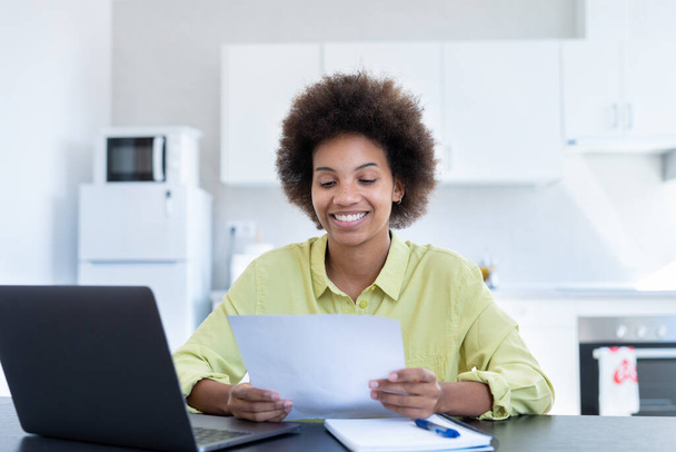 Happy smiling remote working young black female receive postal letter from company office about project report approval. Glad millennial afro american employee reading good news from paper document - Foto, Imagem