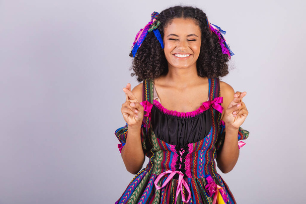Black Brazilian woman wearing festa junina clothes. Fellowship of Saint John. Arraial, fingers crossed, cheering, wishing. - Foto, immagini