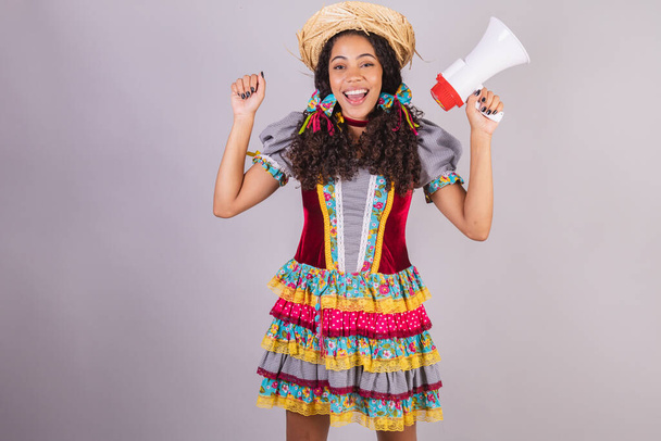 Black, Brazilian woman, wearing June party clothes, fraternization in the name of So Joo, Arraial. Shouting promotion with megaphone - Photo, image