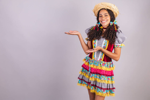 Black, Brazilian woman, wearing June party clothes, fraternization in the name of So Joo, Arraial. presenting product or advertisement on the side - Фото, зображення
