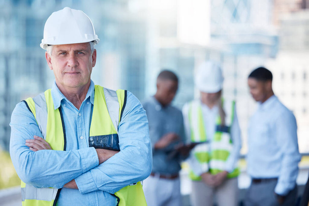 Portrait, arms crossed and a serious man construction worker outdoor on a building site with his team in the background. Management, leadership and confidence with a senior architect standing outside. - Фото, зображення