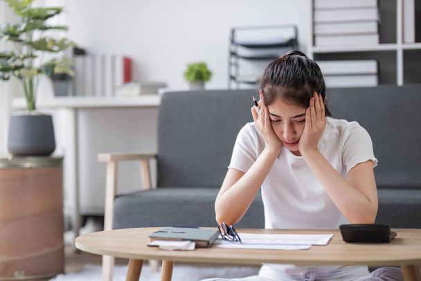 Azji kobieta stres trzymać rachunki w ręku obliczenia wydatków z kalkulator siedzi na kanapie w domu.. - Zdjęcie, obraz